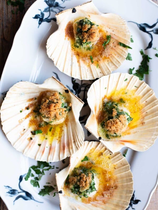 An overhead shot of four scallops in their shells sitting on a white serving platter.